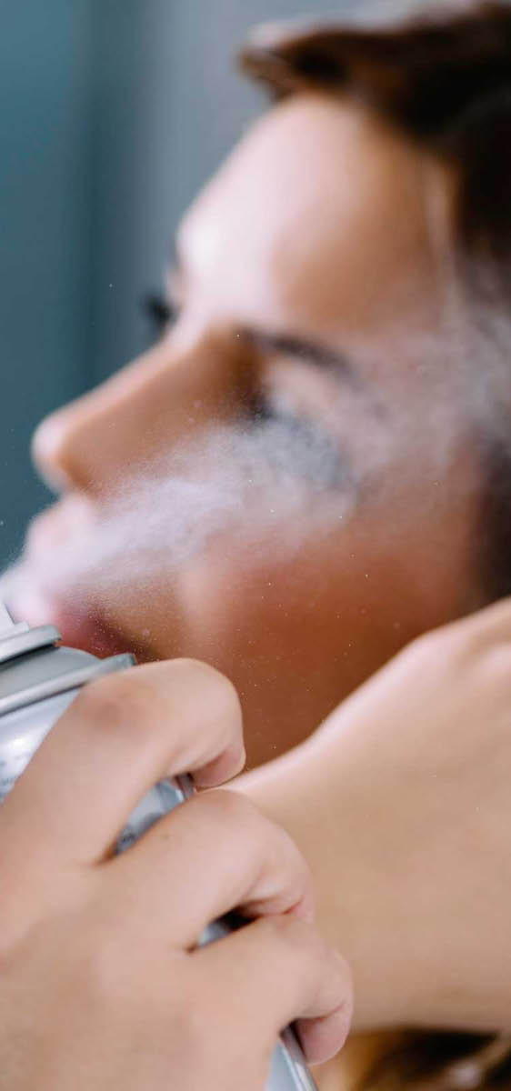 Immagine di una ragazza mora con i capelli lunghi, che si sta applicando la lacca. In primo piano lo spruzzo della lacca